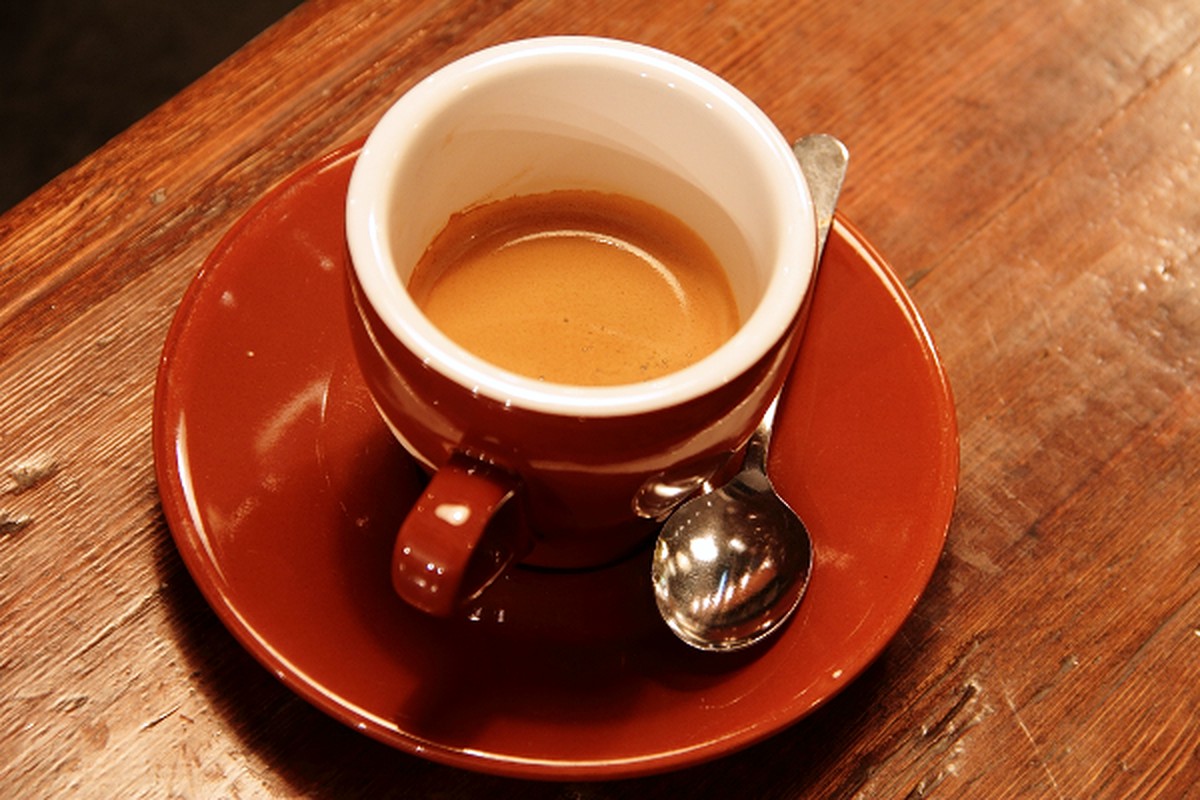 A cup of coffee on a saucer with a spoon on a warm wooden table.