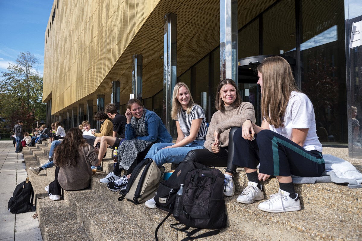 A small group of people sitting and talking outside a modern building in daylight.